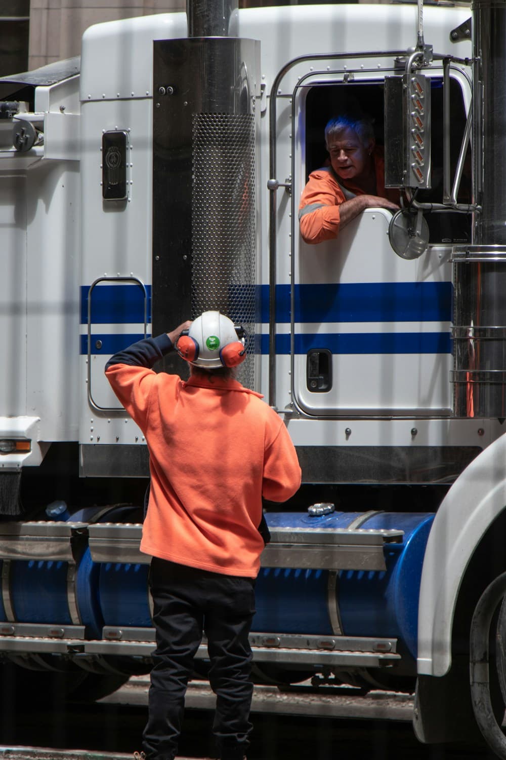 Professional driver in high-visibility gear at a freight truck, coordinating with trained ground crew